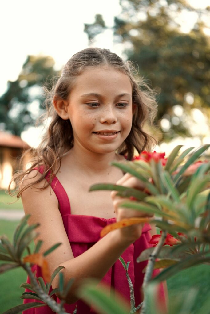 Girl admires a red flower outdoors in a garden.
