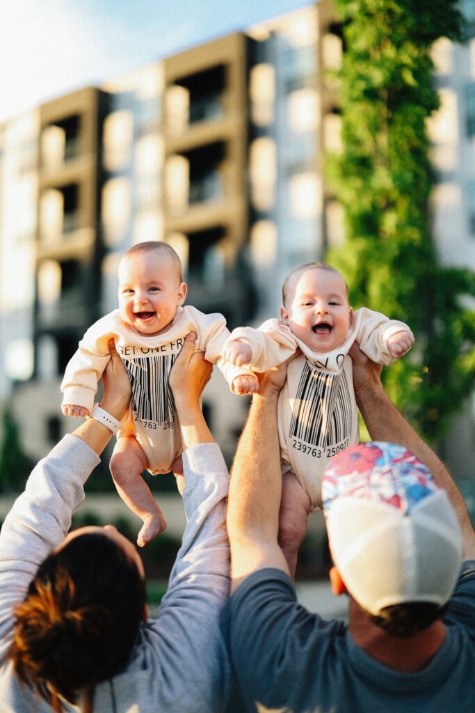 Parents happily lift adorable twin babies.